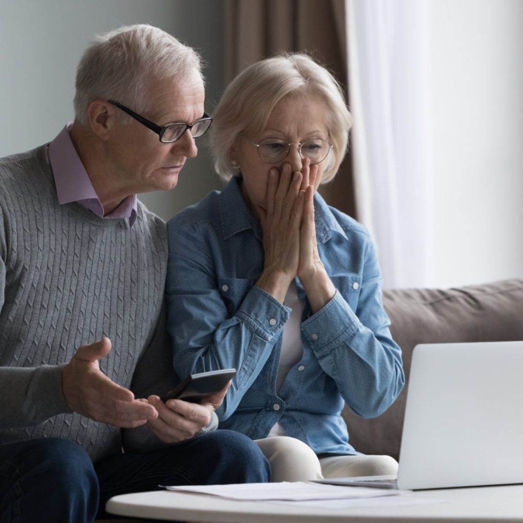 Shocked upset elderly couple getting bad news, finding fraud, money stealing, loss, overspending, financial problem, holding calculator, using laptop, staring at monitor