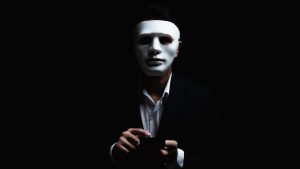A hacker wearing a mask, using a phone.