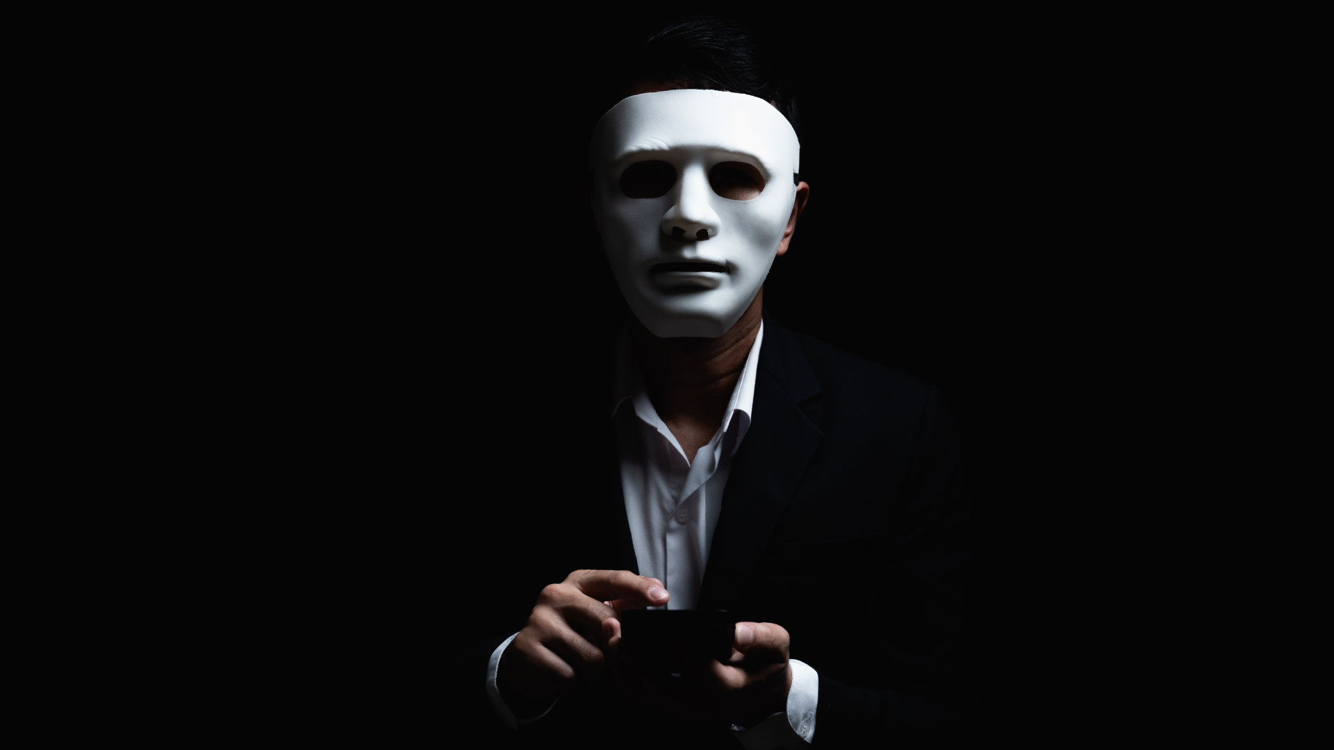 A hacker wearing a mask, using a phone.